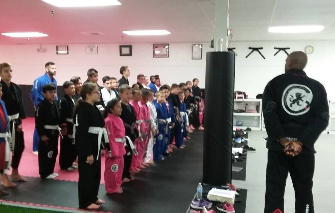 Professor Gideon Ray addressing rows of kids lined up in their gis at the start of a kids martial arts class.